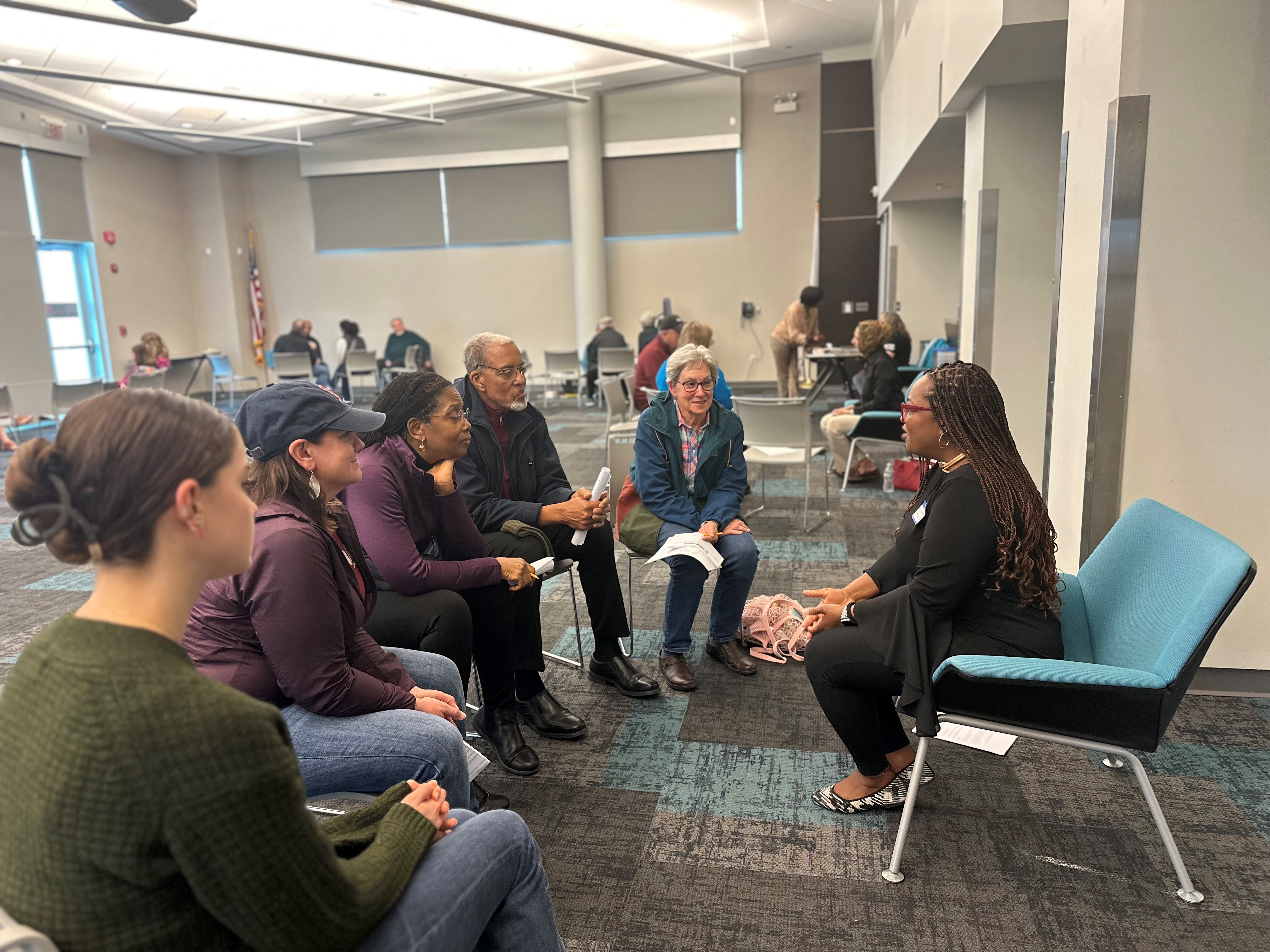 Five people sit on the edges of their seats, listening attentively to a speaker with long brown braided hair at the Human Library program.