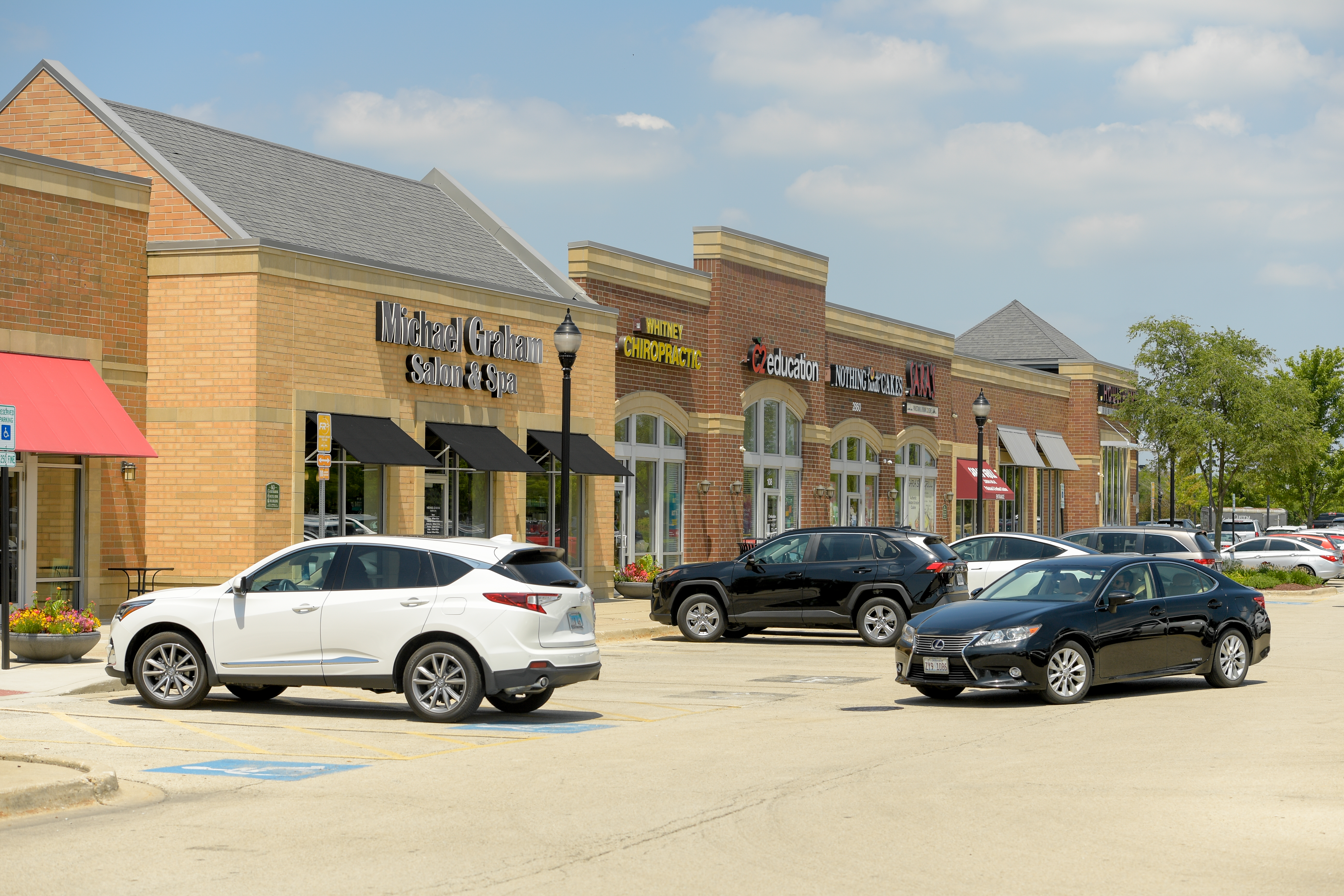 Black car pulling out of parking space at Naperville Crossings mall, with brick storefronts in background.