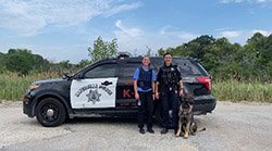 An intern stands in front of a squad car with a K9 officer