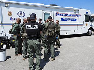 Officers in tactical gear, one with a vest reading Police Negotiator, stand outside a mobile command vehicle.