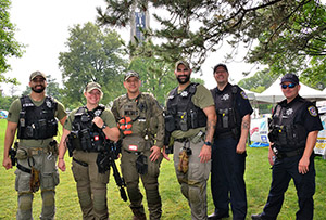 Six officers, some in uniform, some in tactical gear, stand shoulder to shoulder outdoors.