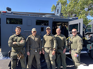 Four Special Response Team members and one tactical medic stand in front of the NPD's armored rescue vehicle.