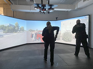 An officer draws her gun while another points his weapon at a virtual reality training simulator.